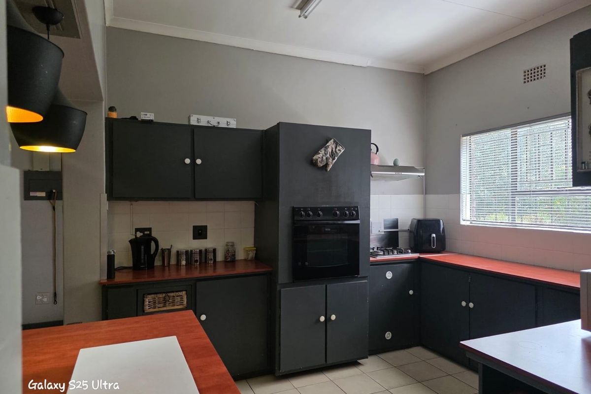 A functional kitchen featuring dark cabinetry, contrasting countertops, built-in oven, and tiled flooring with natural light from a window.