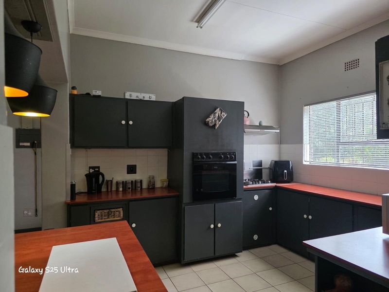 A functional kitchen featuring dark cabinetry, contrasting countertops, built-in oven, and tiled flooring with natural light from a window.