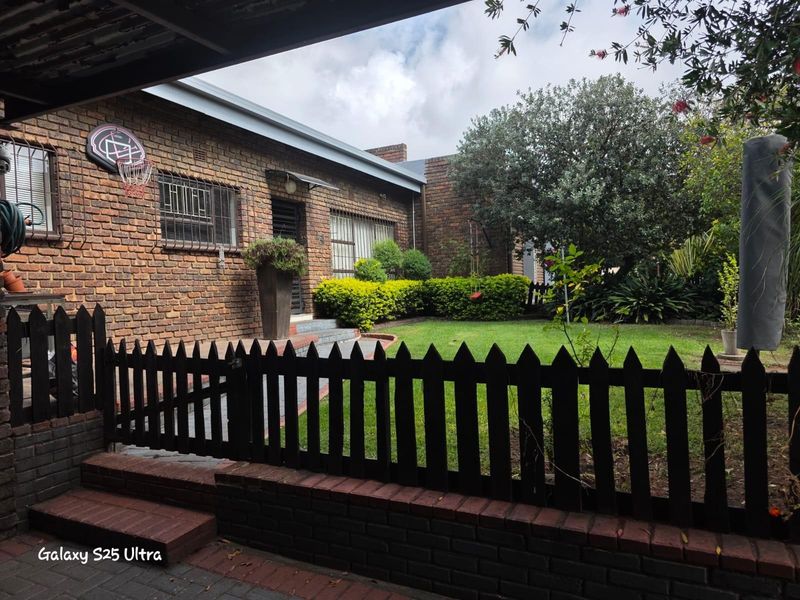 A view of the rear garden featuring a brick facade, a well-maintained lawn, and a black picket fence.