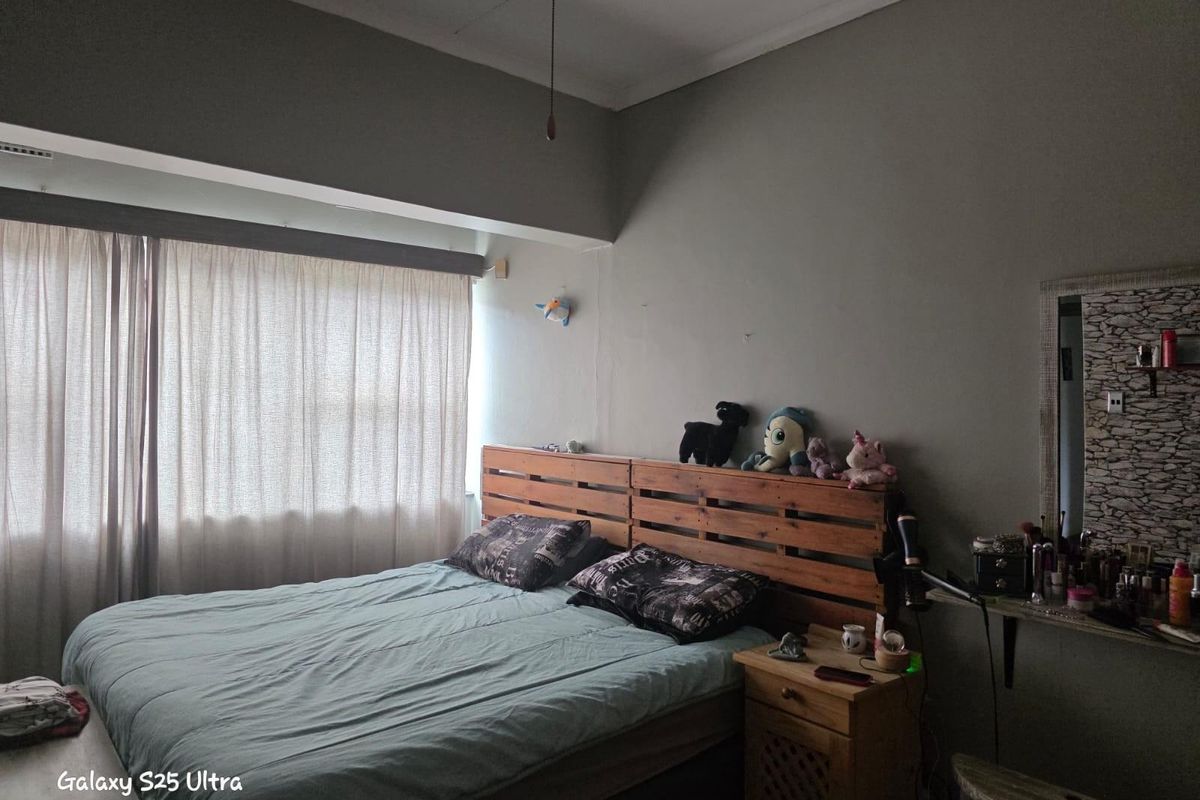 A bedroom featuring a large window with curtains and a neutral wall finish, providing a functional space for rest.