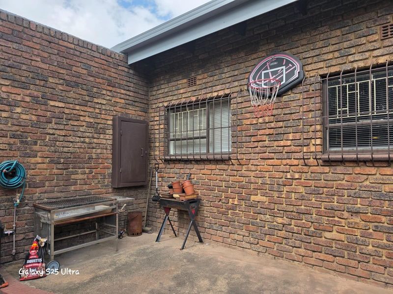 A rear exterior courtyard area featuring exposed brick walls, security bars on windows, and a concrete patio surface.