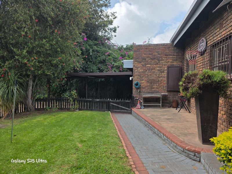 A rear garden area featuring a paved patio, brick exterior wall, and established landscaping with a small wooden fence and lawn.