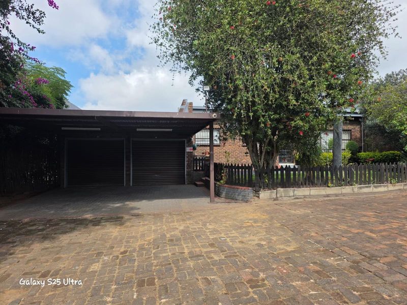 Front exterior view featuring a double carport, brick facade, and paved driveway area with established garden landscaping.