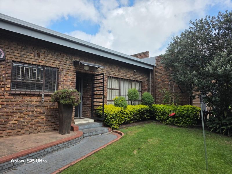 A view of the exterior rear facade featuring face-brick construction, a paved walkway, and a landscaped garden area.