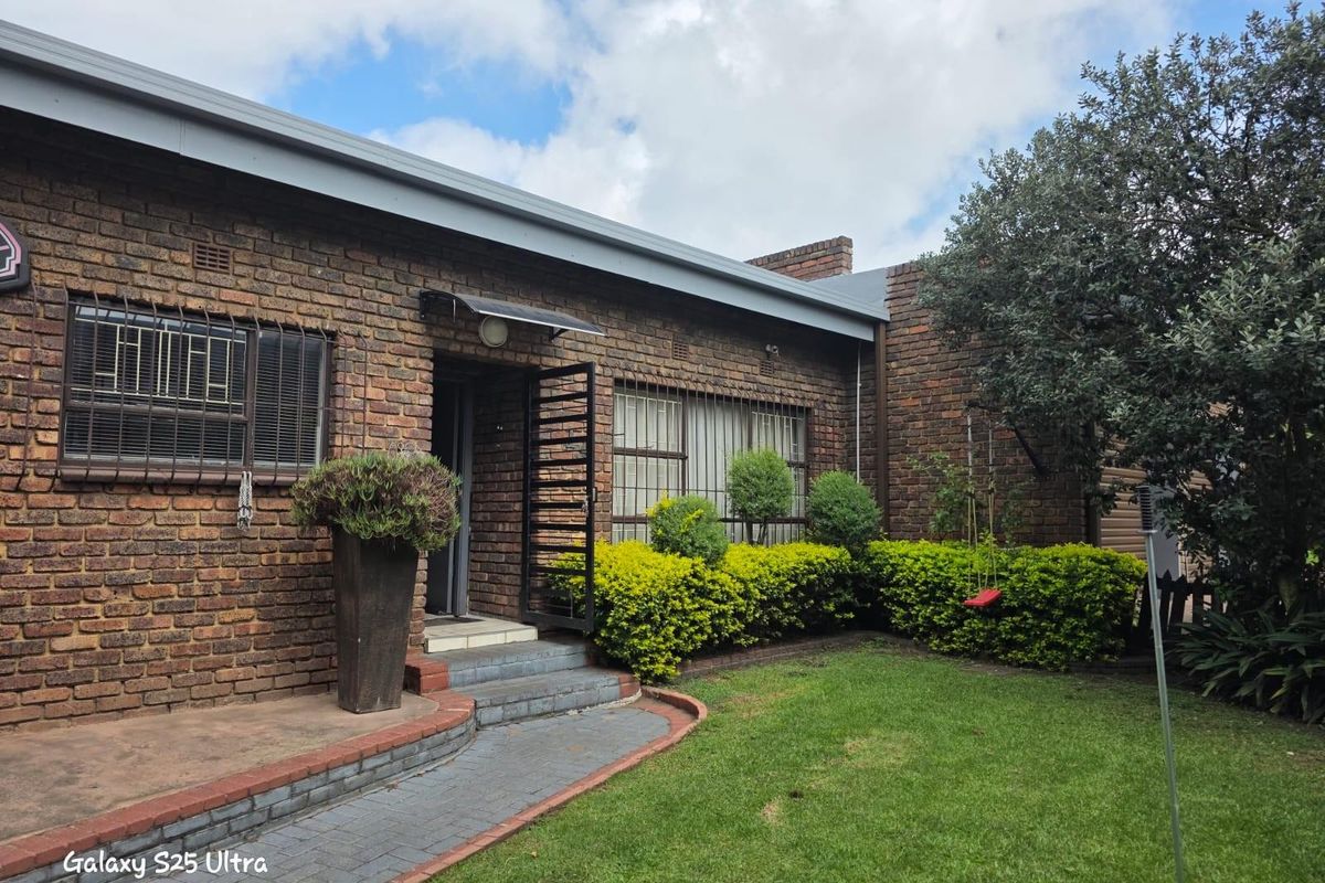 A view of the exterior rear facade featuring face-brick construction, a paved walkway, and a landscaped garden area.