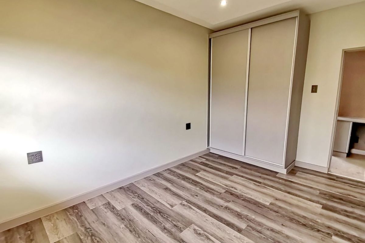 A clean, modern bedroom featuring wood-look laminate flooring, neutral walls, and a built-in sliding door wardrobe.