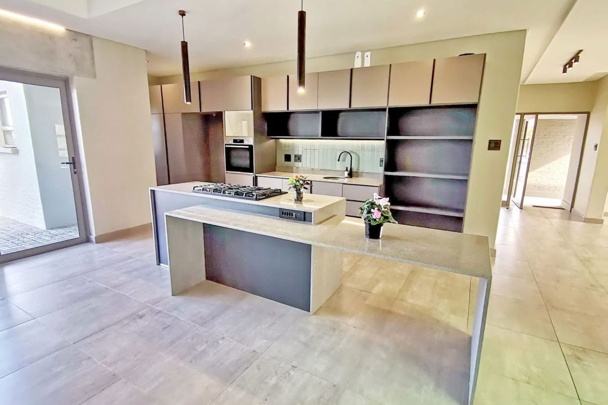 Modern open-plan kitchen featuring sleek cabinetry, a central island with a built-in gas hob, stone countertops, and integrated appliances.