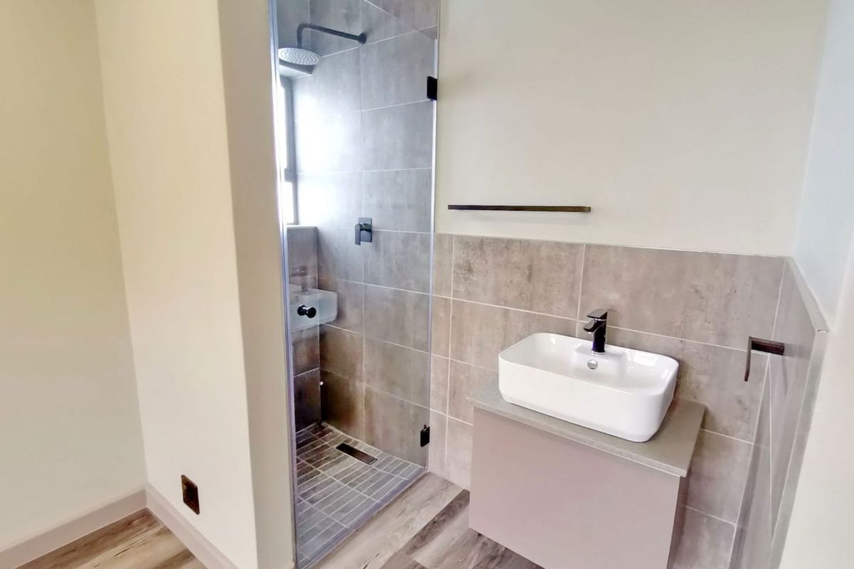 Modern bathroom featuring a glass-enclosed walk-in shower with rainfall showerhead, a contemporary vessel sink vanity, and neutral floor-to-ceiling tiling.