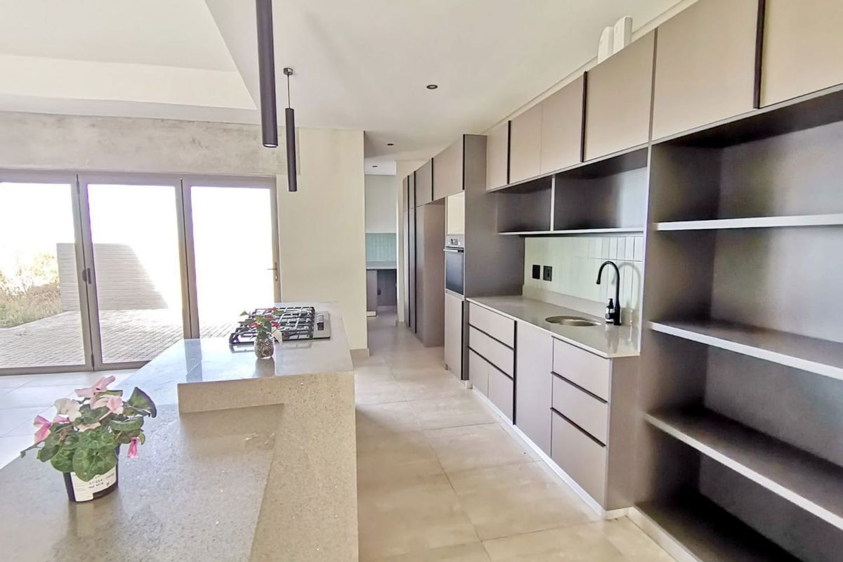 Modern open-plan kitchen featuring a central island with a gas hob, sleek cabinetry, stone countertops, and direct access to the outdoor patio area.