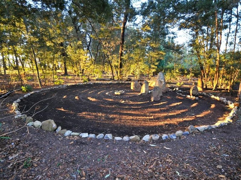A landscaped garden area featuring a circular stone-bordered path and central rock formation set within a wooded environment.