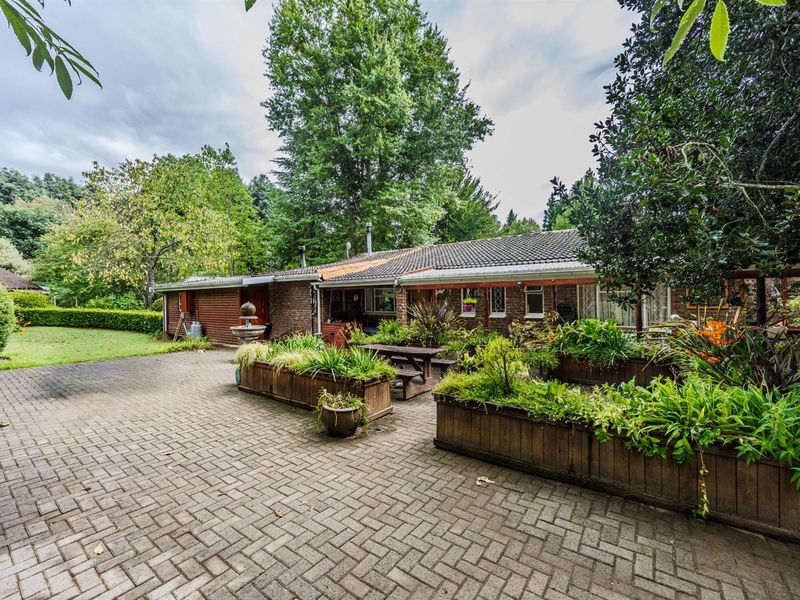 Spacious rear exterior featuring a paved patio area, established garden beds, and direct access to the brick-clad residence.