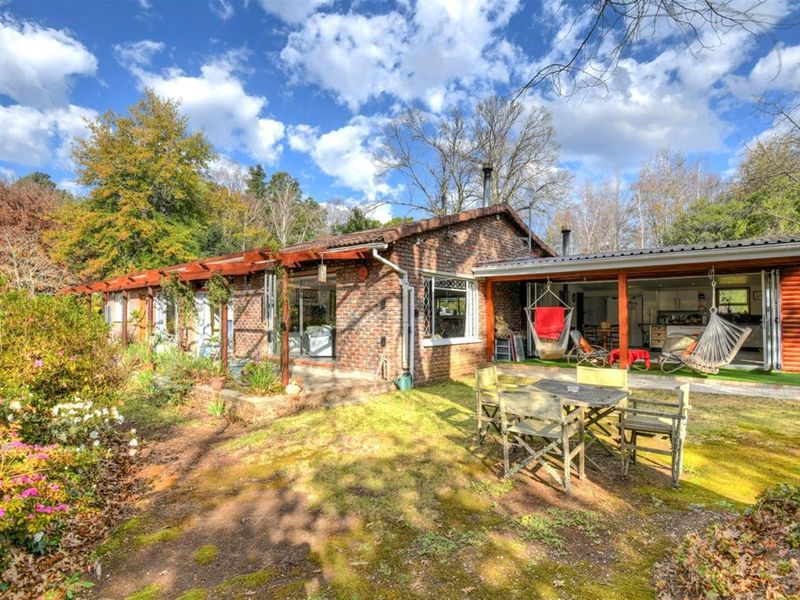 A charming brick-clad rear exterior featuring a covered patio area, timber pergola, and established garden surroundings, offering a peaceful outdoor living space.