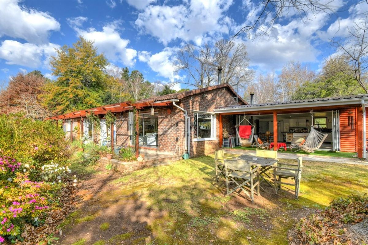 A charming brick-clad rear exterior featuring a covered patio area, timber pergola, and established garden surroundings, offering a peaceful outdoor living space.