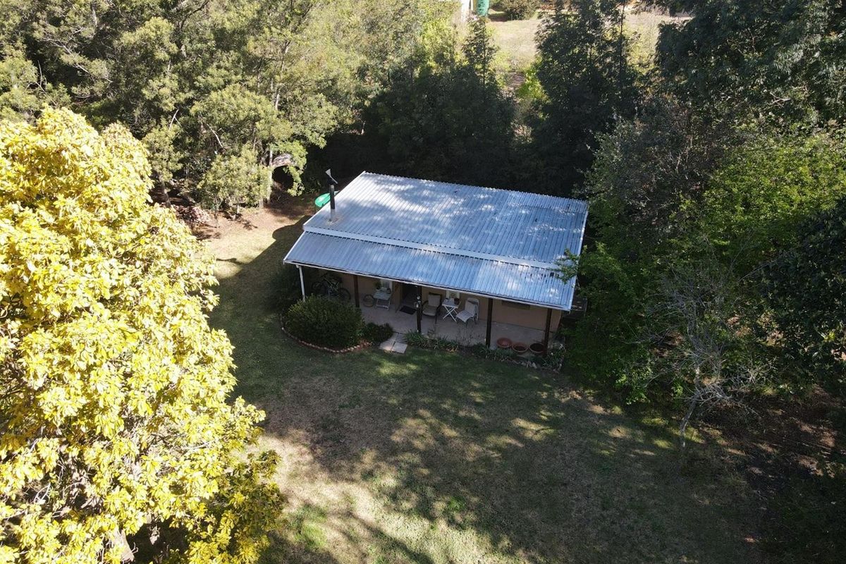 Aerial view of a detached house featuring a corrugated metal roof, a covered front porch, and a spacious surrounding garden with mature trees.
