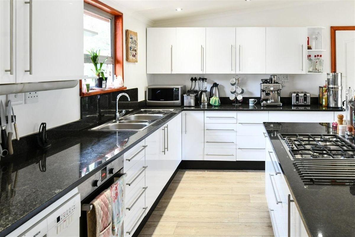 Modern kitchen featuring white cabinetry, contrasting black granite countertops, a central island with a built-in gas hob, and light wood-look flooring.