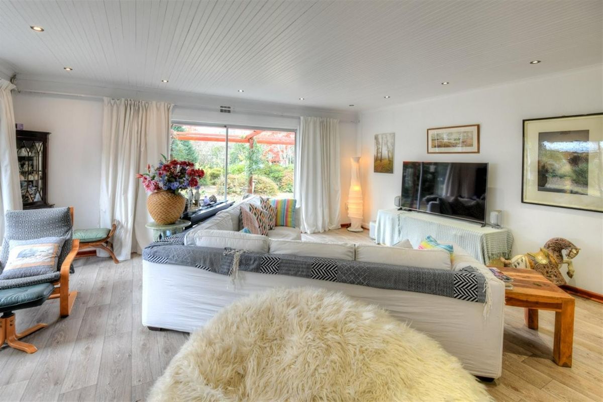 A bright and spacious living room featuring wood-look flooring, recessed ceiling lighting, and large sliding glass doors providing access to the outdoor patio area.