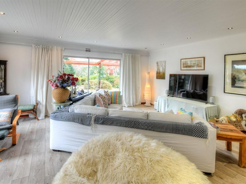 A bright and spacious living room featuring wood-look flooring, recessed ceiling lighting, and large sliding glass doors providing access to the outdoor patio area.