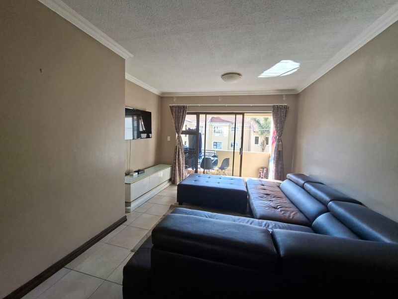 A comfortable living room featuring tiled flooring, crown molding, and sliding glass doors that open onto a private balcony.