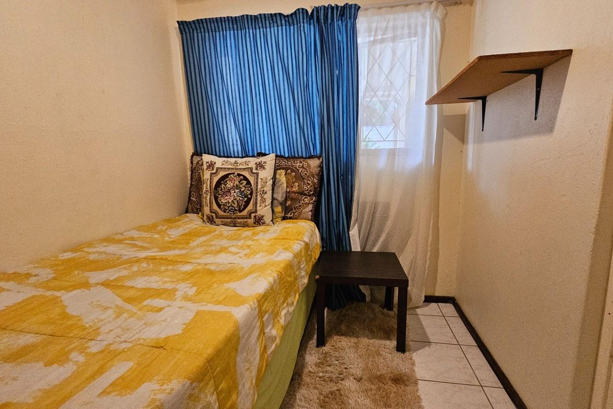 A compact bedroom featuring tiled flooring, a window with curtain tracks, and a wall-mounted shelf.