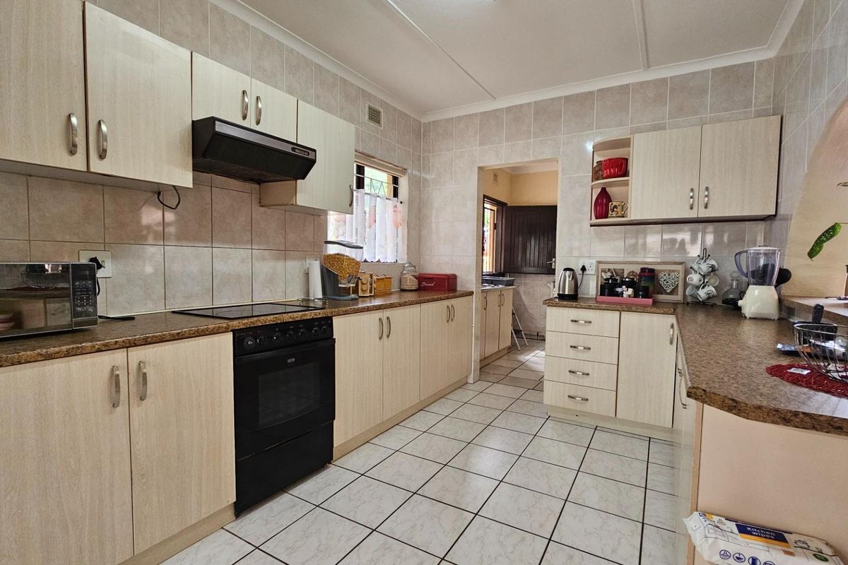 A functional kitchen featuring light-toned cabinetry, tiled walls, a built-in oven with extractor fan, and a breakfast bar area.