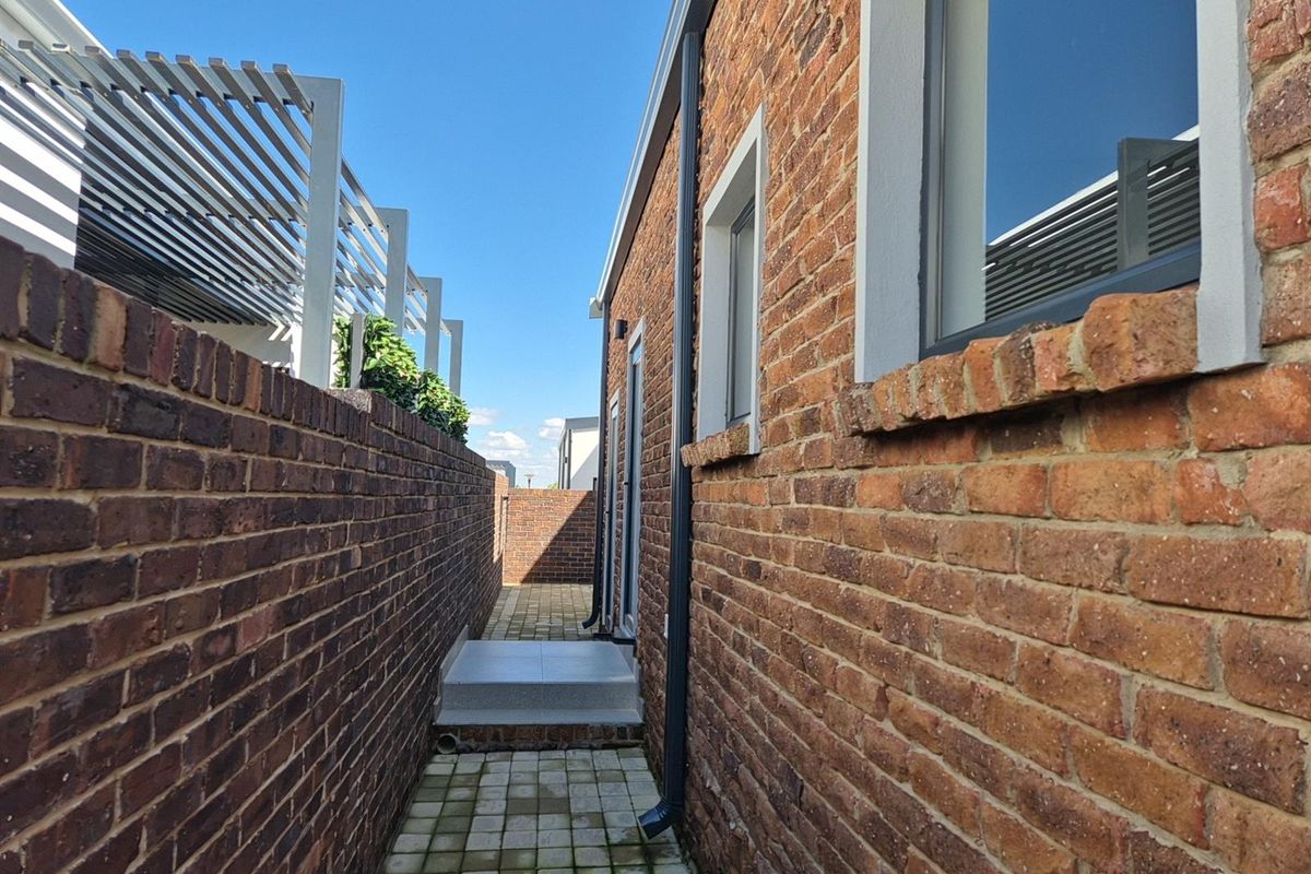 A side passage featuring exposed brick walls, paved flooring, and a small concrete step leading to a rear entrance.