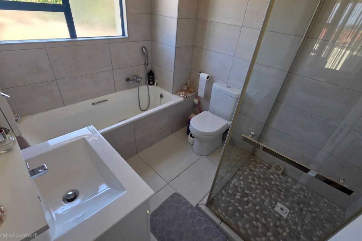 Modern bathroom featuring a built-in bathtub, separate glass-enclosed shower with pebble-style flooring, vanity basin, and toilet with neutral wall tiling.