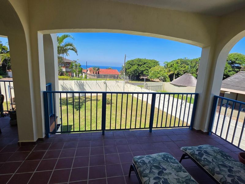 Covered balcony featuring tiled flooring and metal railings, offering an open view of the garden and surrounding neighborhood.