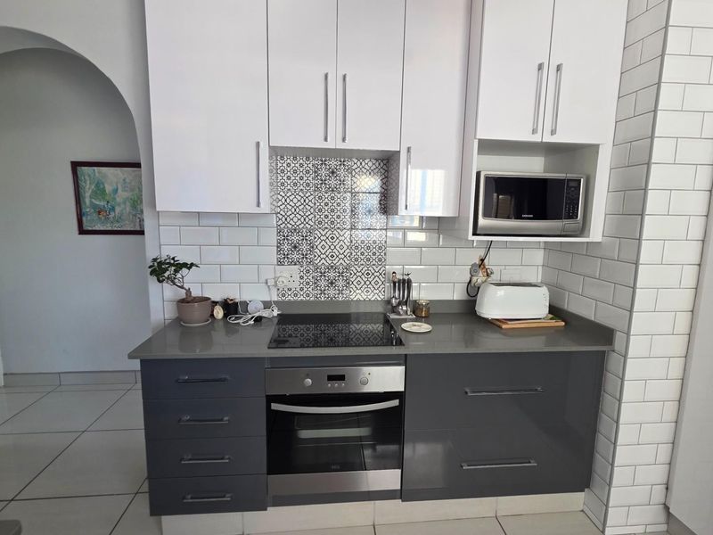 Modern kitchen featuring two-tone cabinetry, stone countertops, built-in oven, electric hob, and decorative tiled backsplash with subway tile wall finishes.