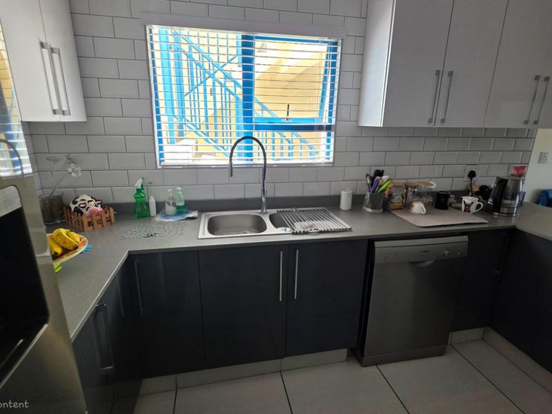 Modern kitchen featuring dark grey cabinetry, contrasting white subway tile backsplash, stainless steel sink, and integrated dishwasher.
