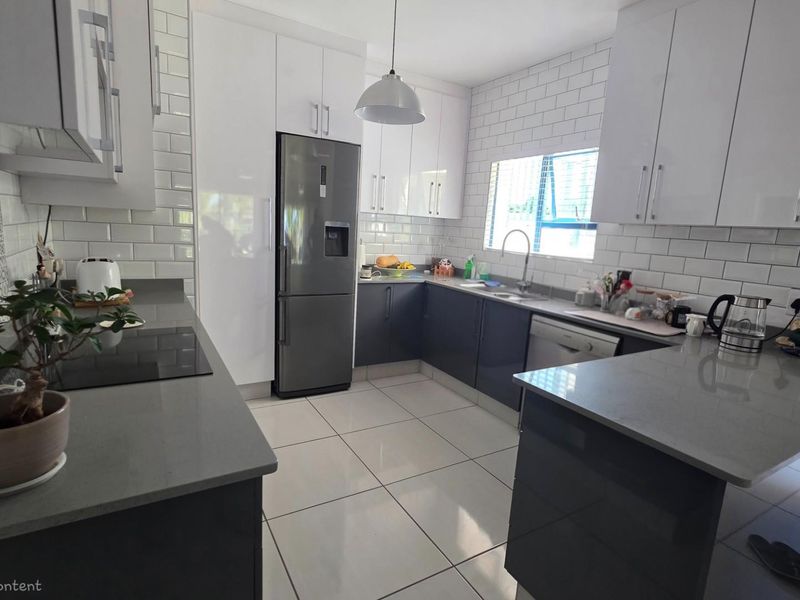Modern kitchen featuring sleek grey cabinetry, white subway tile backsplash, stone countertops, and integrated appliances in a clean, functional layout.
