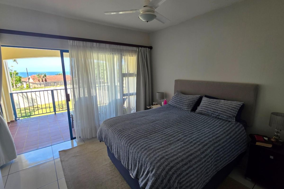 A bedroom featuring tiled flooring, a ceiling fan, and sliding glass doors that open onto a private balcony with ocean views.