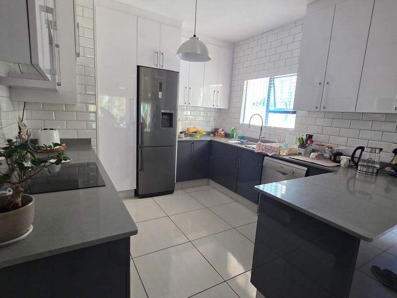 Modern kitchen featuring sleek two-tone cabinetry, stone countertops, subway tile backsplash, and integrated-style appliances in a functional U-shaped layout.