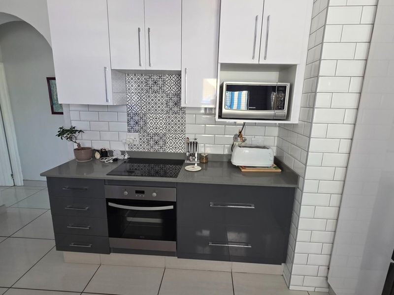 Modern kitchen featuring two-tone cabinetry, subway tile backsplash with decorative accent tiles, stone countertops, built-in oven, and electric hob.