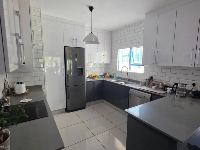 Modern kitchen featuring sleek white and dark grey cabinetry, stone countertops, subway tile backsplash, and integrated stainless steel appliances.