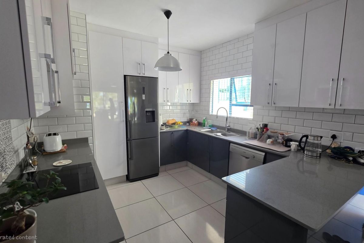 Modern kitchen featuring sleek white and dark grey cabinetry, stone countertops, subway tile backsplash, and integrated stainless steel appliances.