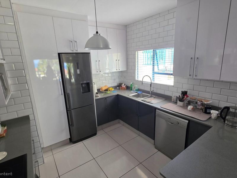 Modern kitchen featuring white upper cabinetry, dark lower cabinets, subway tile backsplash, stone countertops, and integrated stainless steel appliances.