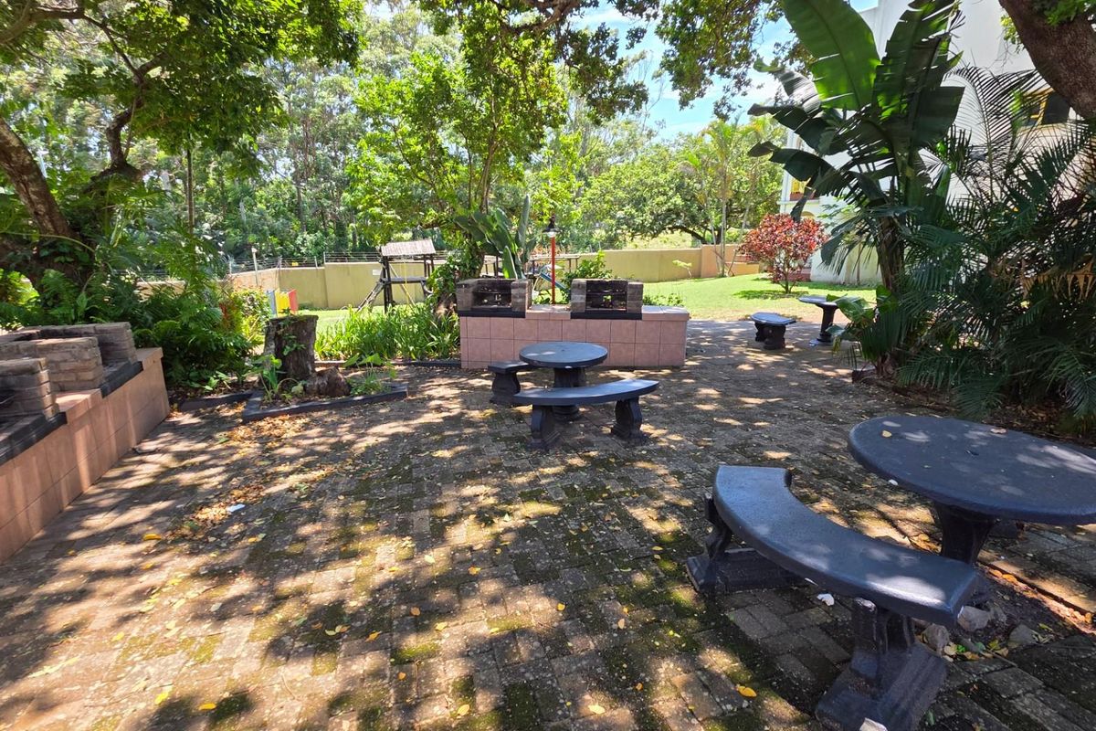 Communal outdoor entertainment area featuring built-in brick braai facilities and paved patio space set within a landscaped garden environment.