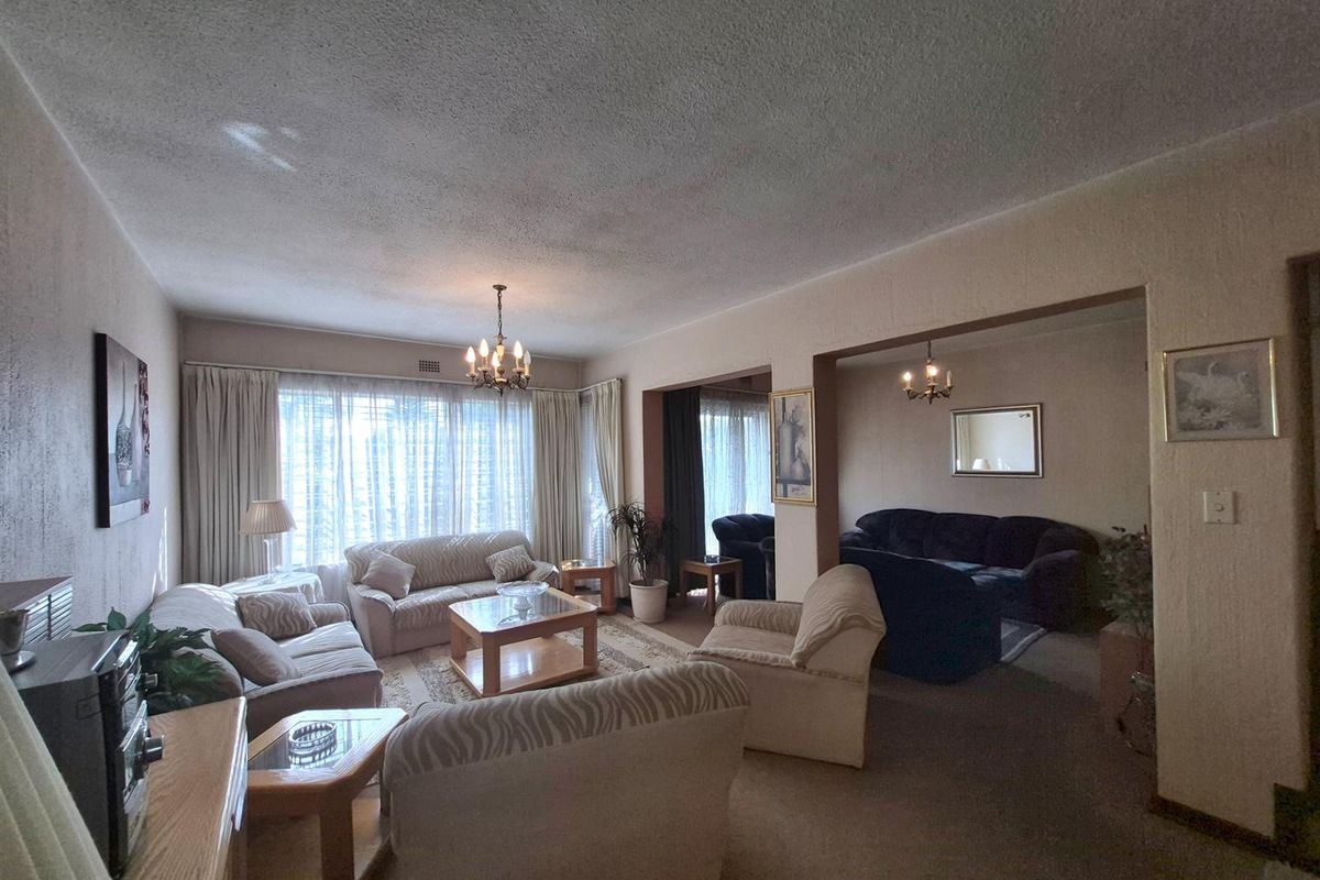 Spacious living area featuring textured ceilings, a central chandelier, and large windows allowing for natural light, with carpeted flooring throughout.