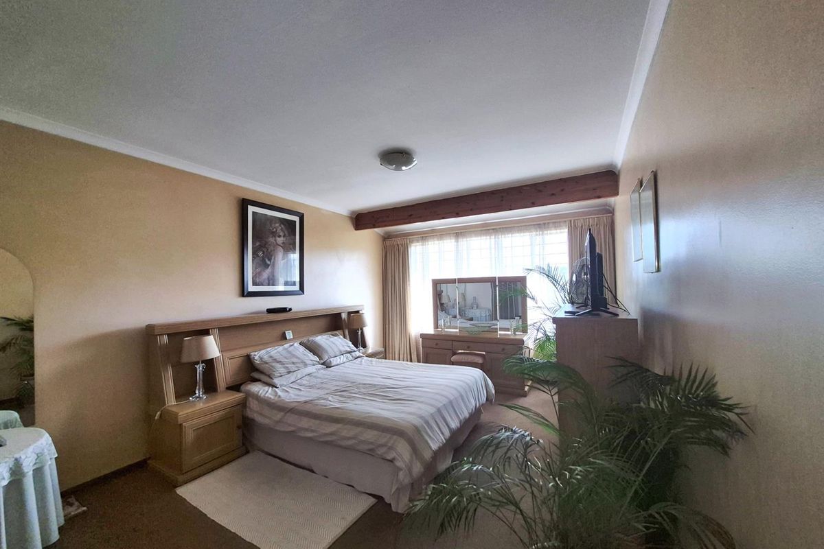 A spacious bedroom featuring an exposed timber ceiling beam, neutral wall finishes, and carpeted flooring, offering a comfortable and functional living space.
