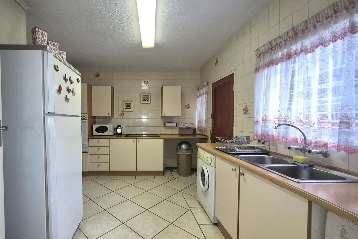 A functional kitchen featuring tiled flooring, laminate countertops, double stainless steel sink, and ample built-in cabinetry with a tiled splashback.