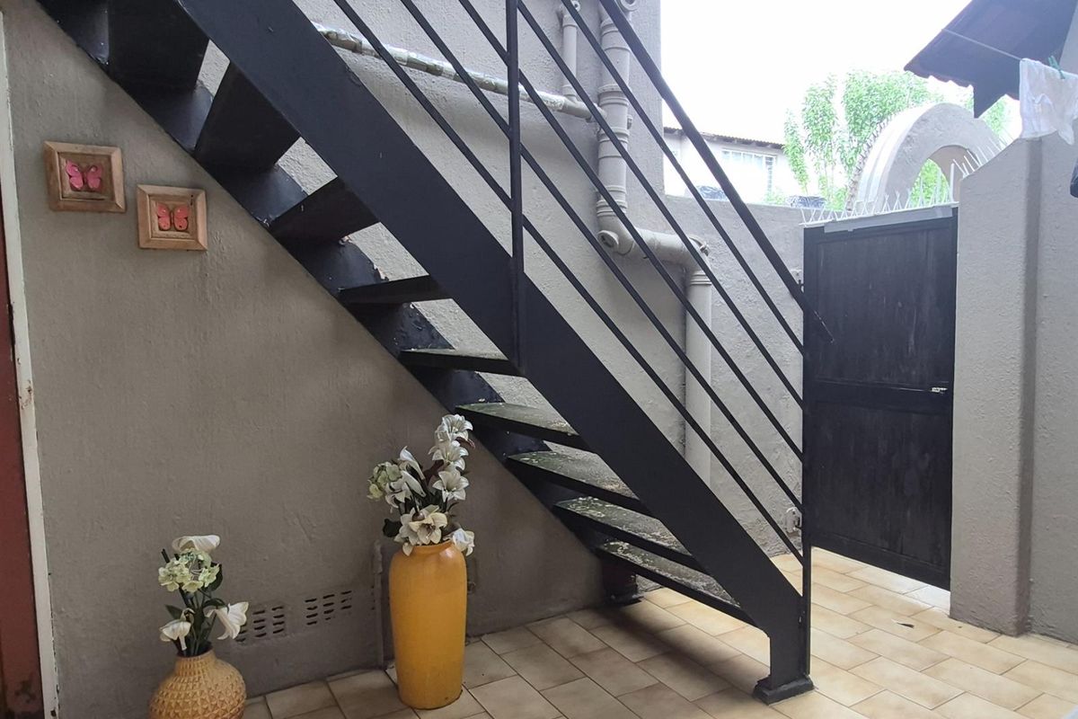Rear exterior area featuring a metal staircase, tiled flooring, and a security gate, providing access to the upper level of the townhouse.