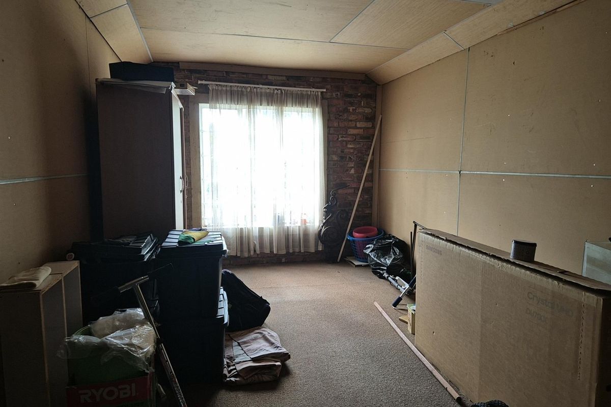 A utility room or bedroom space featuring exposed brickwork, unfinished wall paneling, and carpeted flooring, currently used for storage.