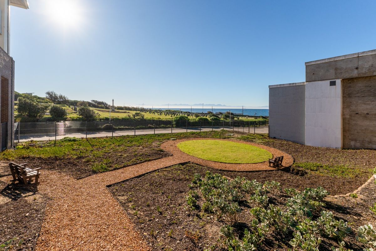 A rear garden area featuring a gravel pathway, circular lawn, and wire fencing, offering scenic coastal and landscape views.