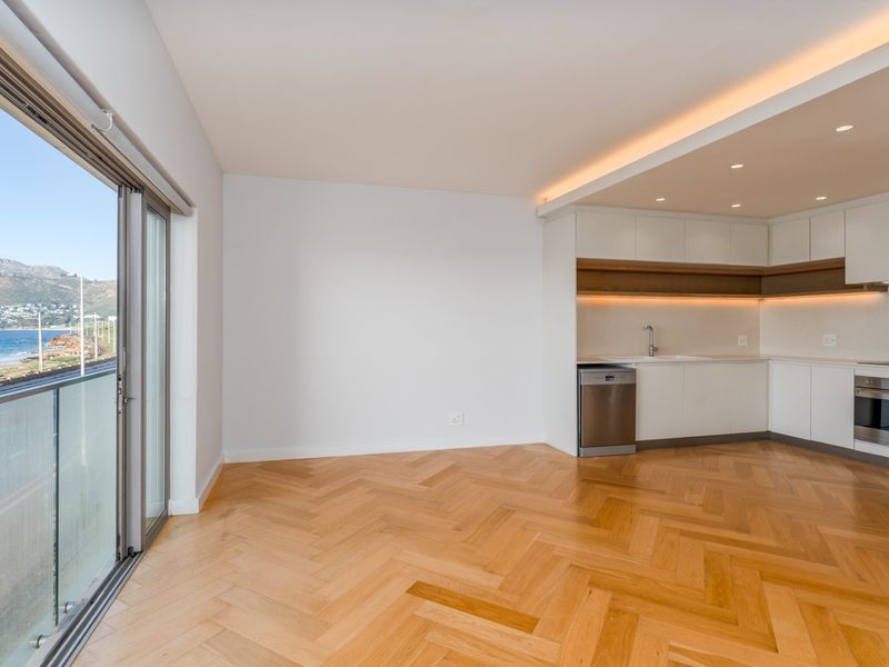 Modern open-plan kitchen and living area featuring high-quality herringbone timber flooring, sleek cabinetry, integrated appliances, and expansive sliding doors opening to a scenic coastal view.