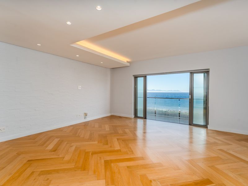 Spacious, light-filled living area featuring premium herringbone timber flooring, recessed ceiling lighting, and large sliding doors opening to a scenic ocean view balcony.