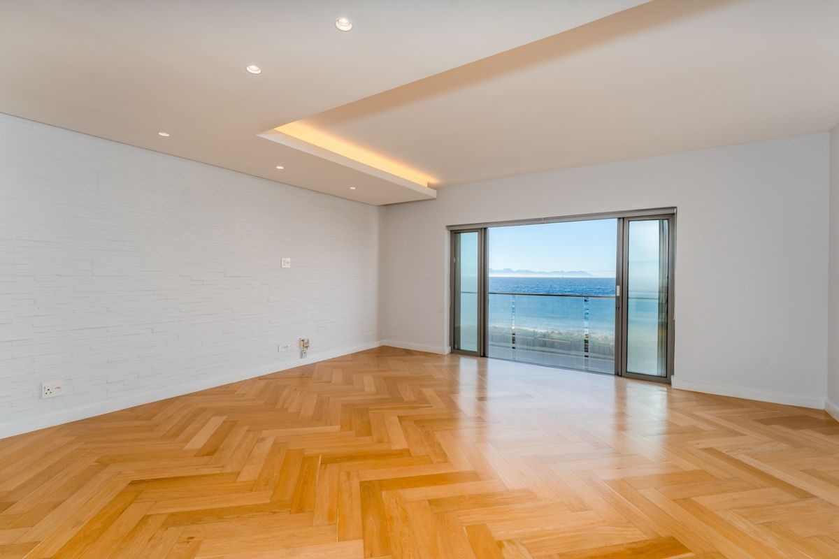 Spacious, light-filled living area featuring premium herringbone timber flooring, recessed ceiling lighting, and large sliding doors opening to a scenic ocean view balcony.