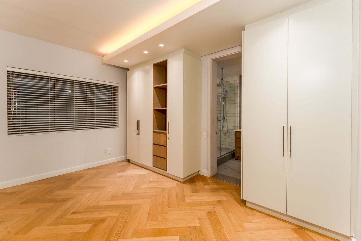 A modern bedroom featuring herringbone timber flooring, extensive built-in cabinetry, recessed ceiling lighting, and direct access to an en-suite bathroom.