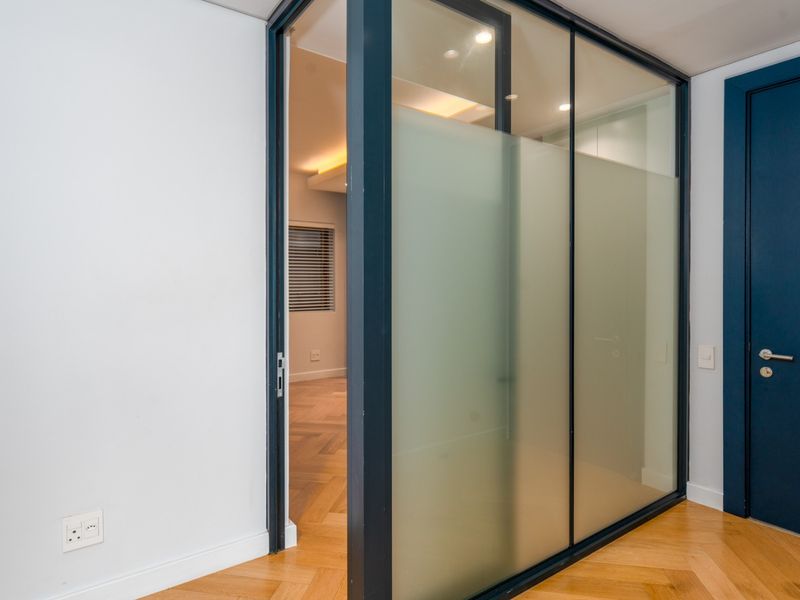 A modern hallway featuring elegant herringbone timber flooring, a sleek frosted glass sliding door, and recessed ceiling lighting, creating a bright and contemporary transition space.
