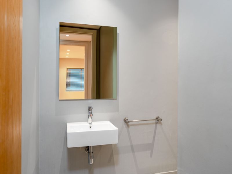 A clean and modern guest bathroom featuring a wall-mounted basin, chrome fixtures, and a minimalist mirror.