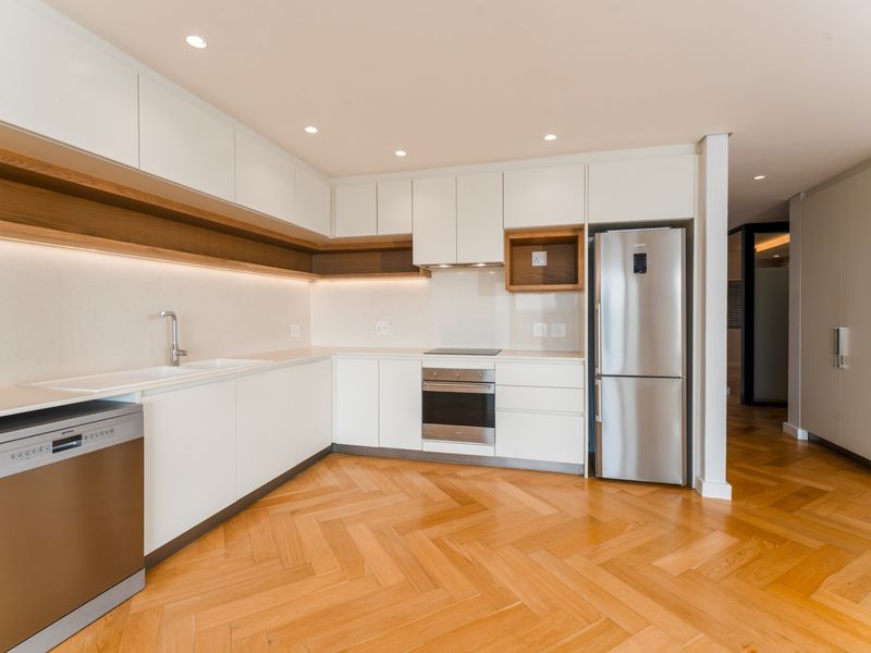 Modern kitchen featuring sleek white cabinetry, stone countertops, integrated appliances, and elegant herringbone timber flooring with warm under-cabinet lighting.